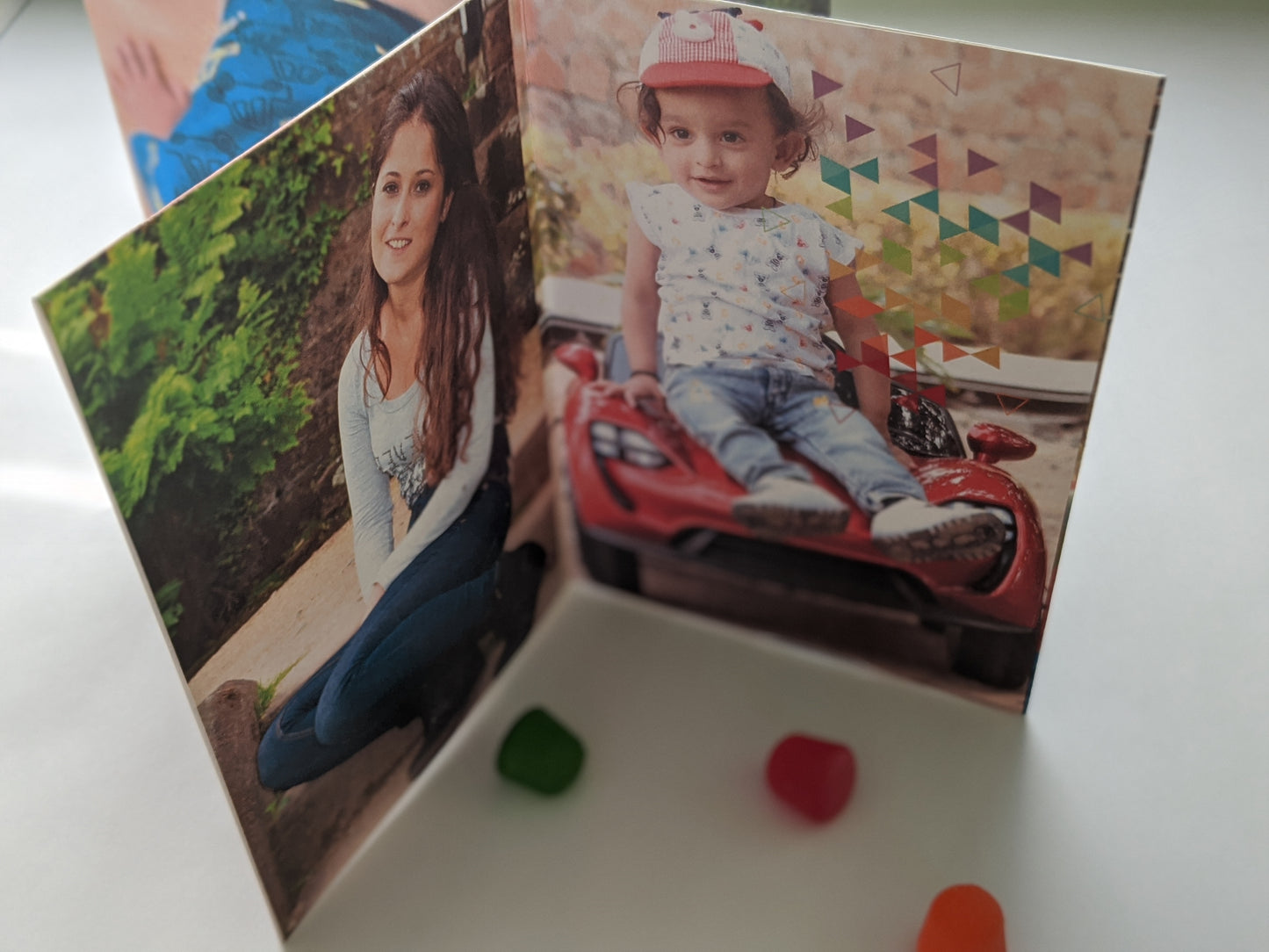 Centerpiece on a white background with colorful candy pieces. The panels show a small child sitting on a toy car and a young adult crouching in a garden both looking at the camera and smiling.