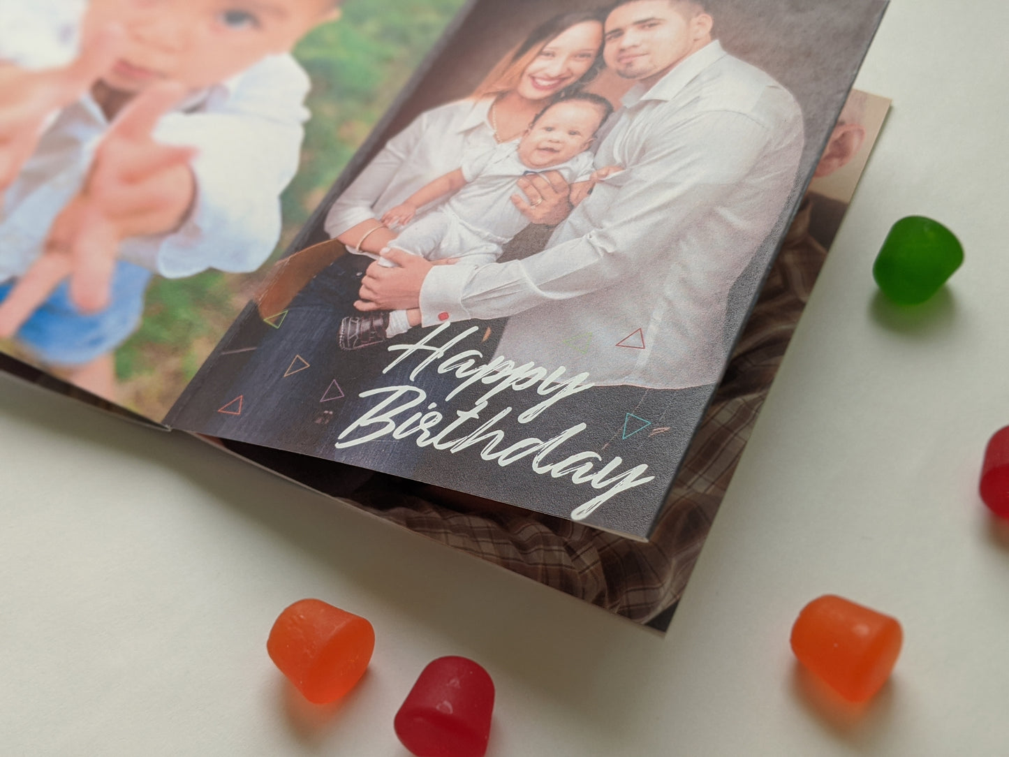 Centerpiece laying flat on a white background with colorful candy. The panels show a small child reaching their hands toward the camera and a young family portrait smiling and looking at the camera collaged with the words Happy Birthday.