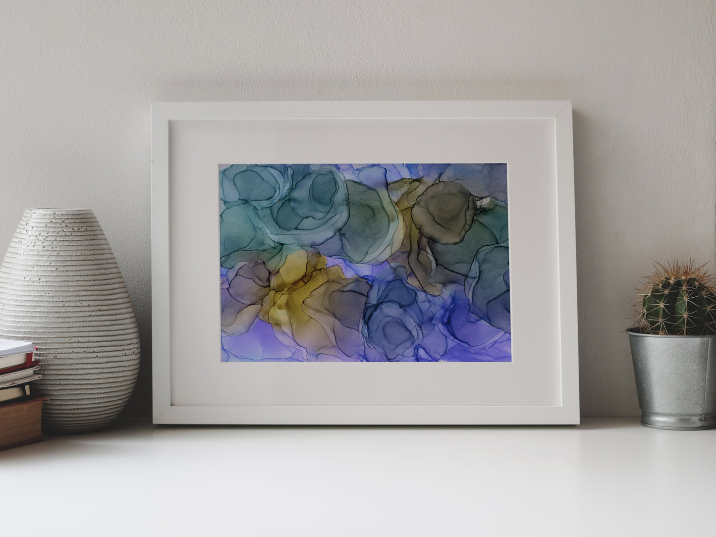 Digital mockup of Moonglade framed in white on a white table top, leaning up against a white background, surrounded by a vase, stack of books, and tiny cactus in a pail.