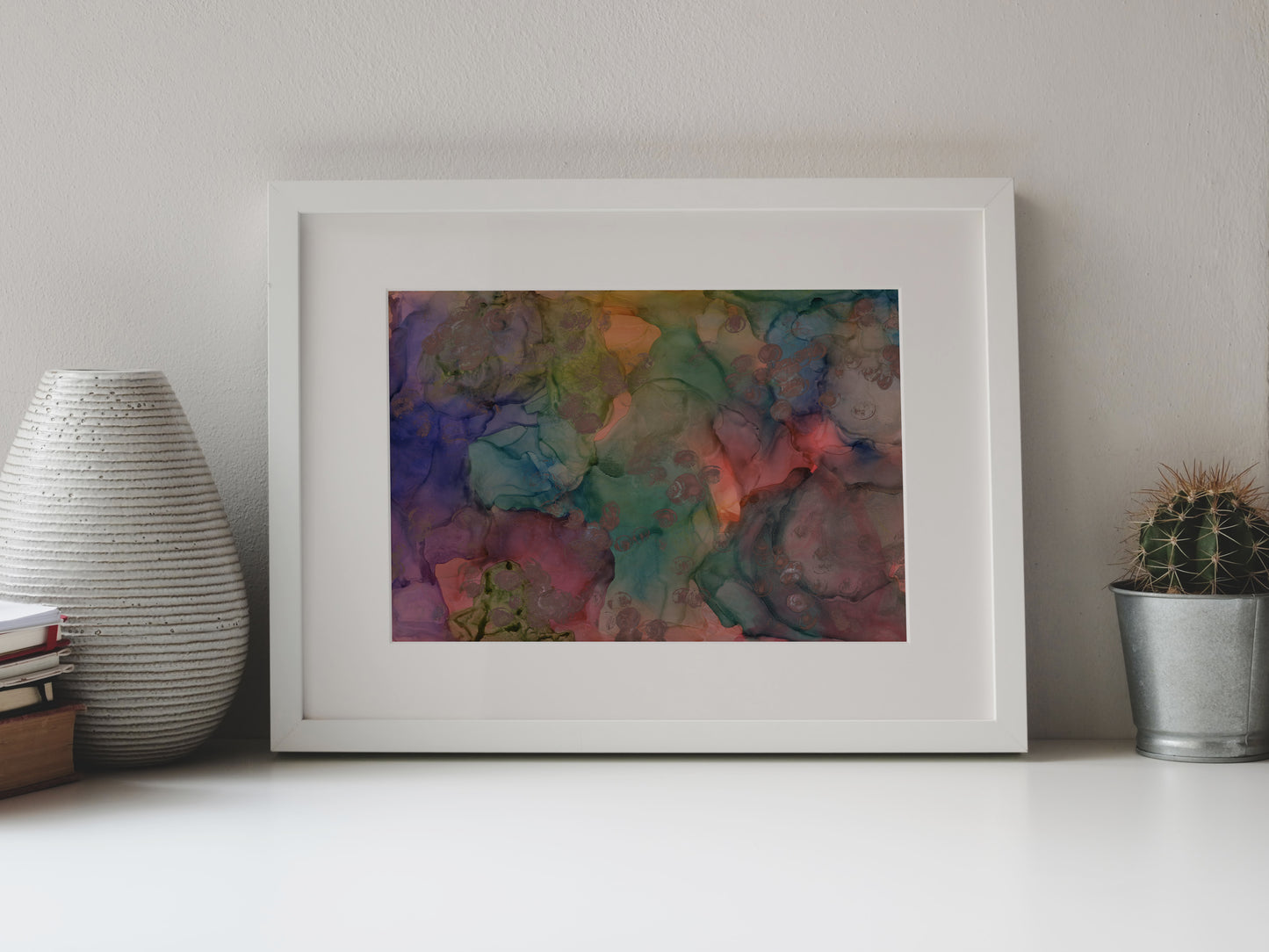 Digital mockup of Coming to the Surface framed in white on a white table top, leaning up against a white background, surrounded by a vase, stack of books, and tiny cactus in a pail.