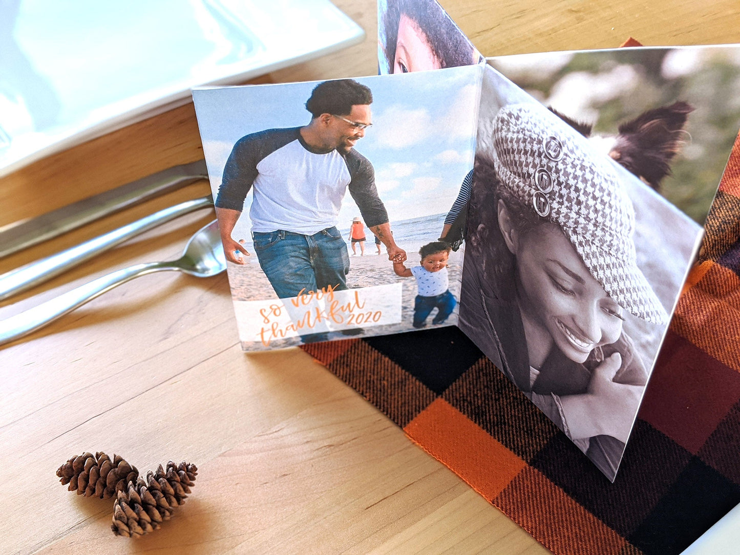 Centerpiece sitting on a wooden table surrounded by a plate, utensils, pinecones and a checkered napkin in fall colors. The panels show two adults holding hands with a toddler walking along a beach and the words so very thankful, and also a young adult smiling at something off camera.
