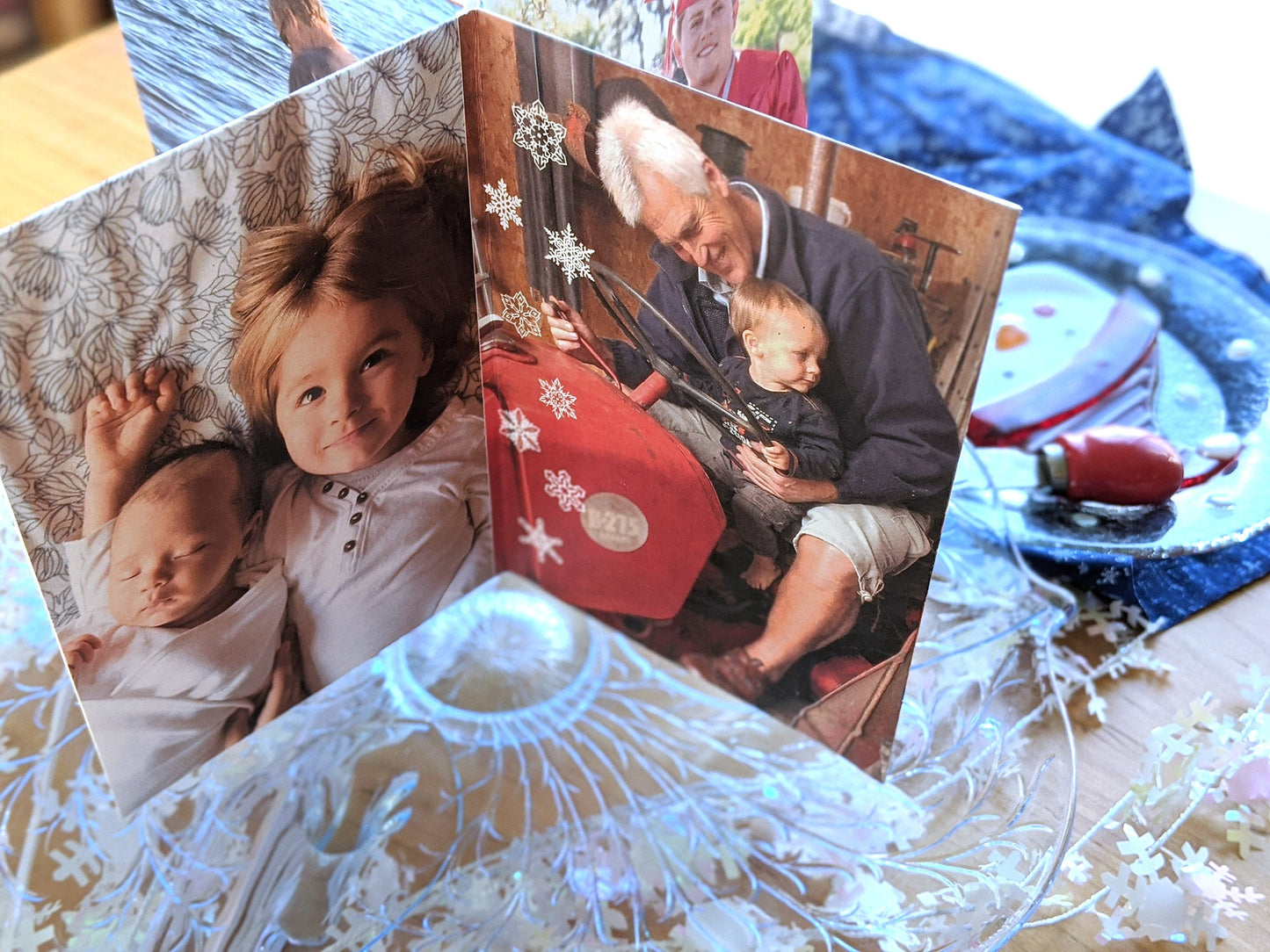 Centerpiece sitting on a glass dessert tray among a snowman plate, snowflake fabric, and snowflake confetti. The panels show a preschooler laying next to a newborn staring up at the camera and a grandfather sitting on a tractor with a toddler.