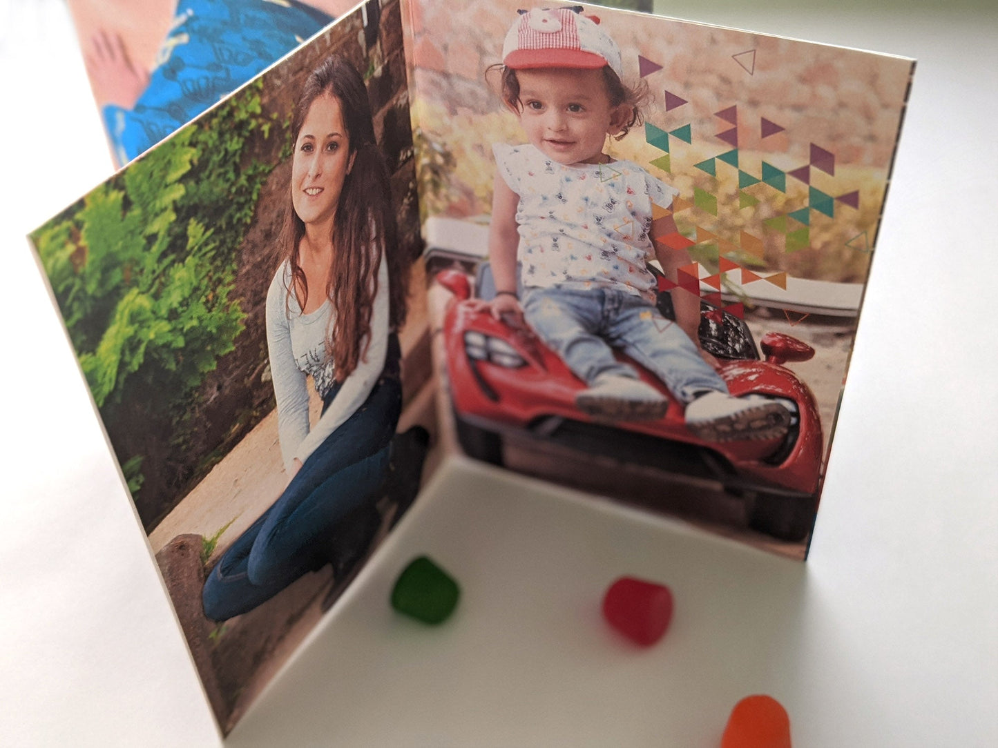 Centerpiece on a white background with colorful candy pieces. The panels show a small child sitting on a toy car and a young adult crouching in a garden both looking at the camera and smiling.