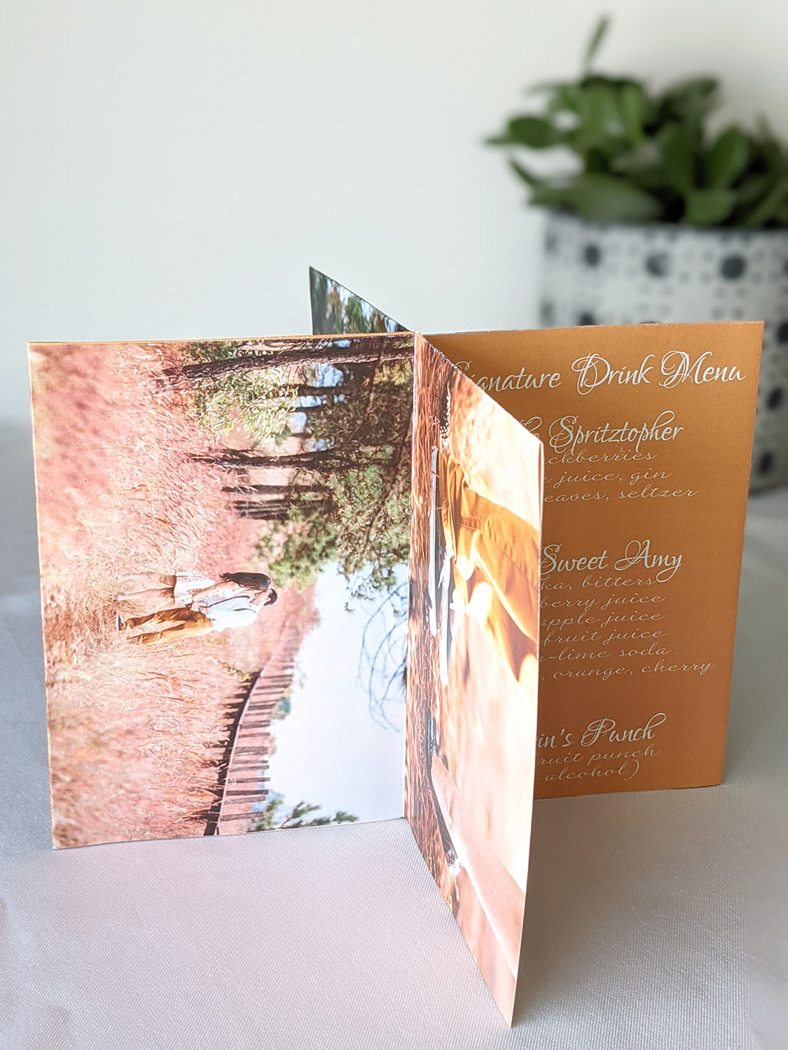 Centerpiece sitting on a white background with an engagement photo of a couple kissing in a field and a signature drink menu list.