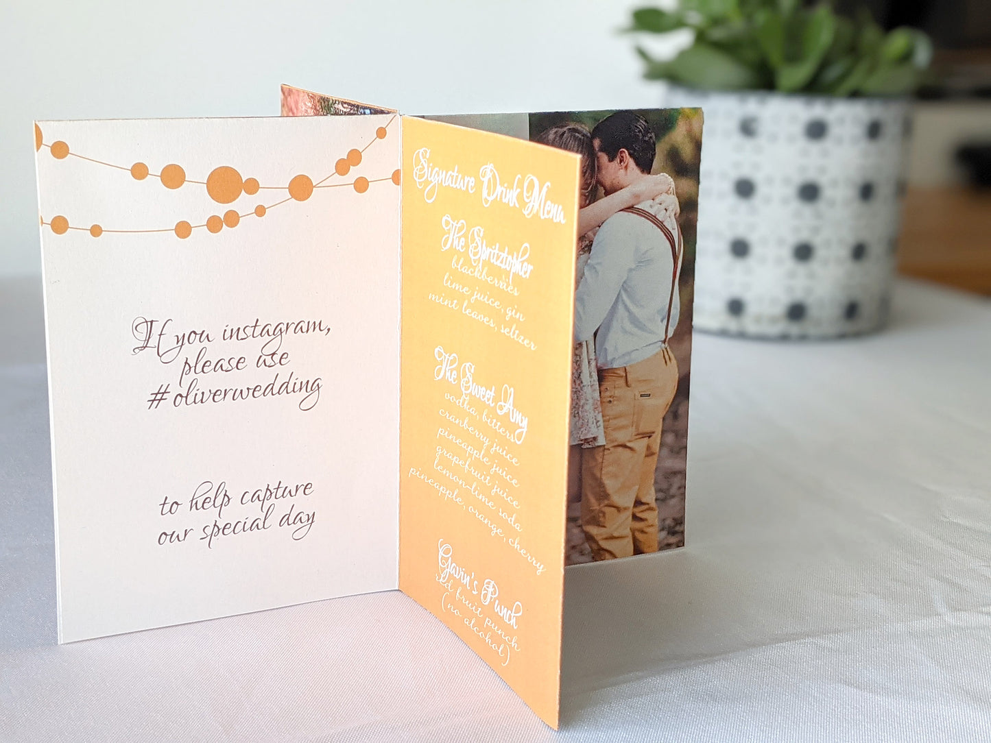 Centerpiece sitting on a white background with panels showing an engagement photo, the signature drink menu, and social media hashtag instructions.