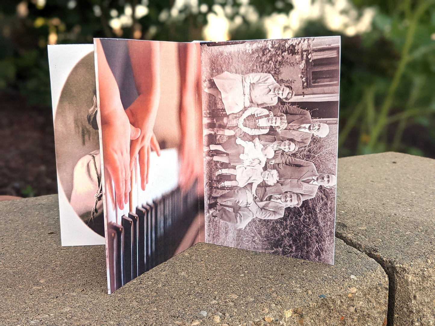 Centerpiece sitting on landscape stone with panels showing Celebration of Life, a sepia family photo posed in a front yard, and two sets of hands playing piano.