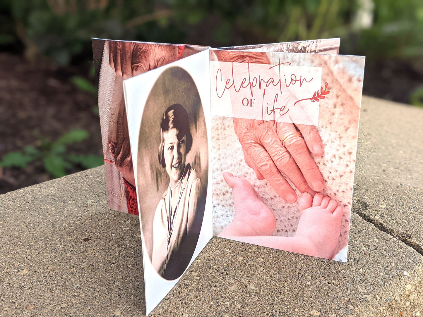 Centerpiece sitting on landscape stone with panels showing Celebration of Life, a sepia school portrait in a rounded frame, and a photo of a wrinkled hand reaching for baby toes on a crocheted blanket.