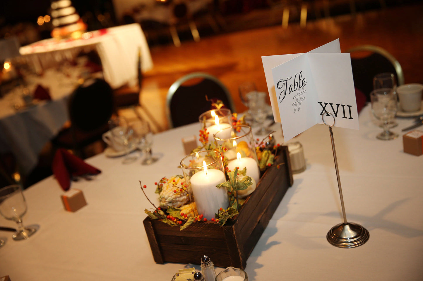 A zoomed in view of a similar banquet table with fall decor. The centerpiece shows two more panels of the table number designation with roman numerals and Table # on a standalone pick.