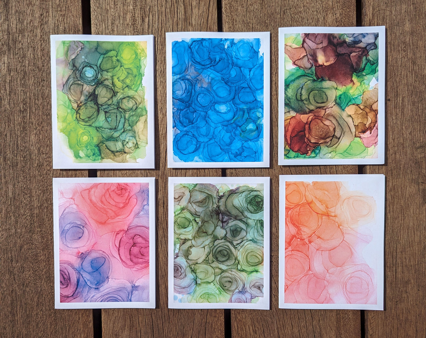 Hand holding six greeting cards fanned out with green and yellow leaves in the background.