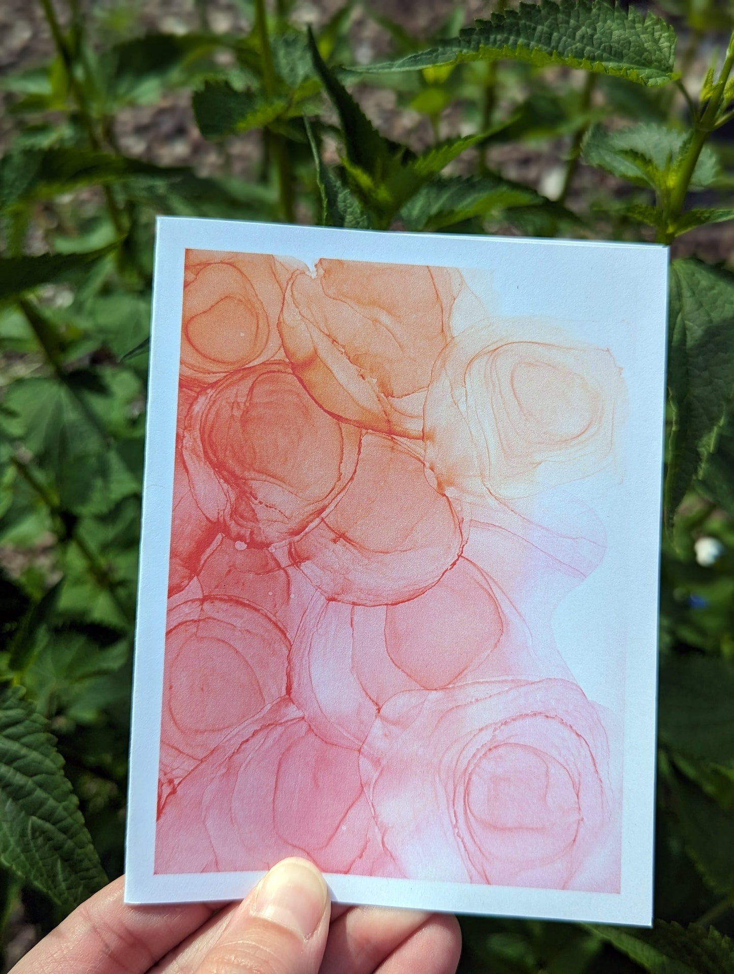 Hand holding a greeting card with green leaves in the background.