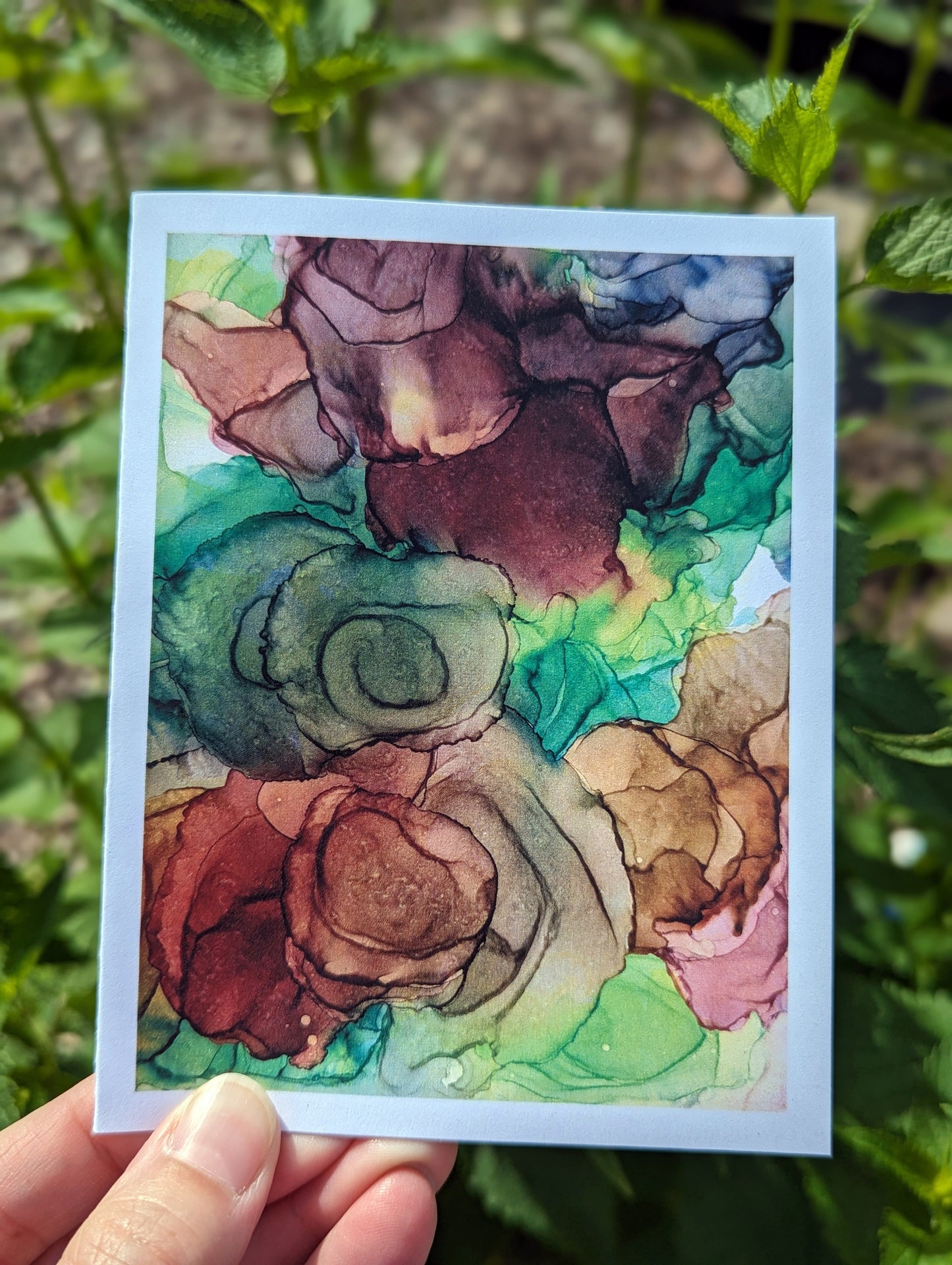 Hand holding a greeting card with green leaves in the background.