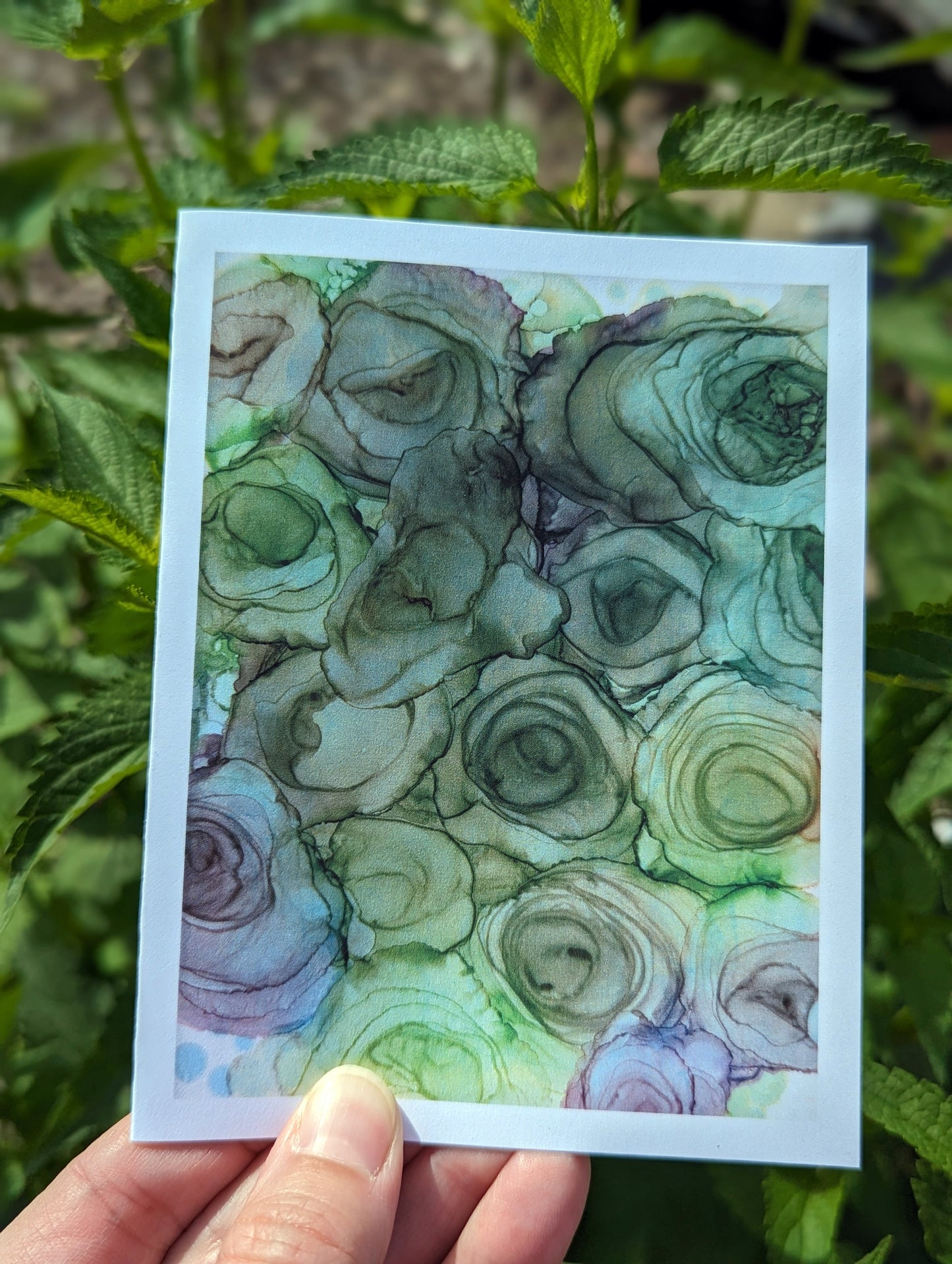 Hand holding a greeting card with green leaves in the background.