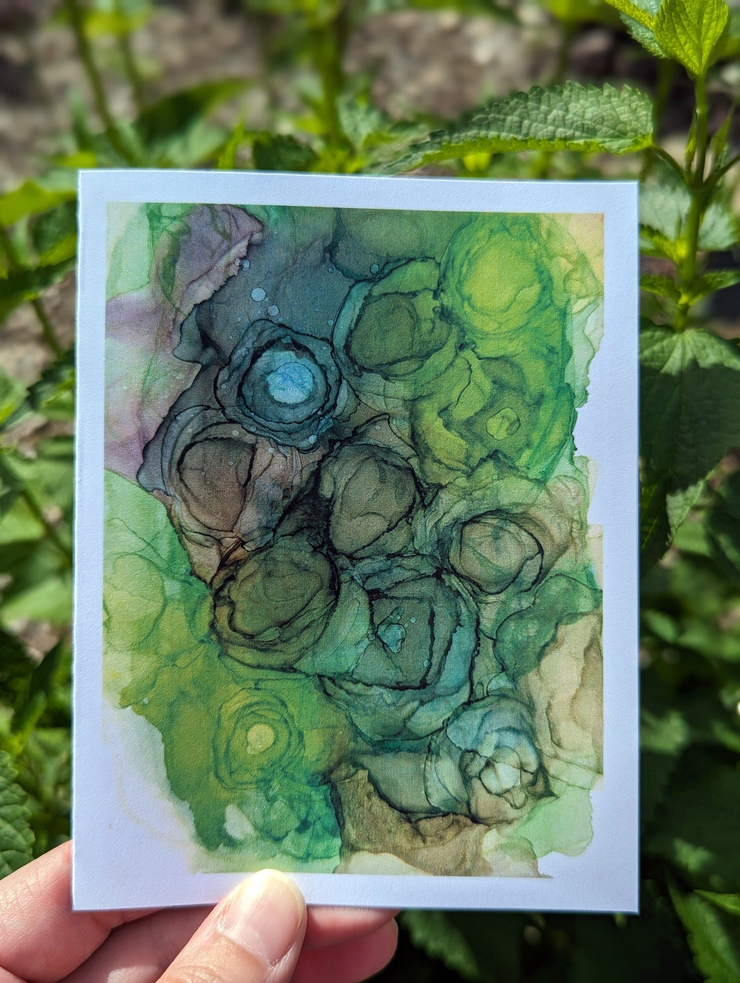 Hand holding a greeting card with green leaves in the background.