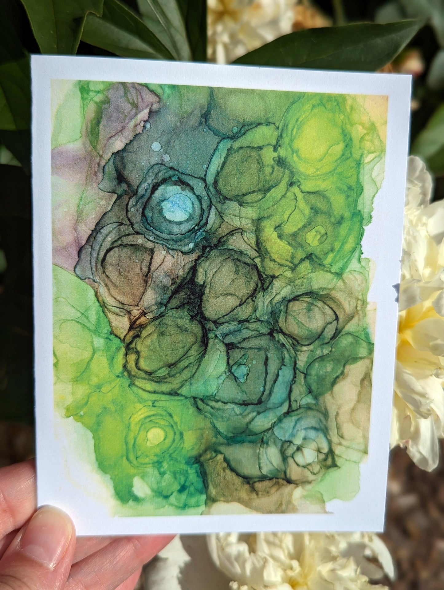 Hand holding a greeting card with green leaves in the background.