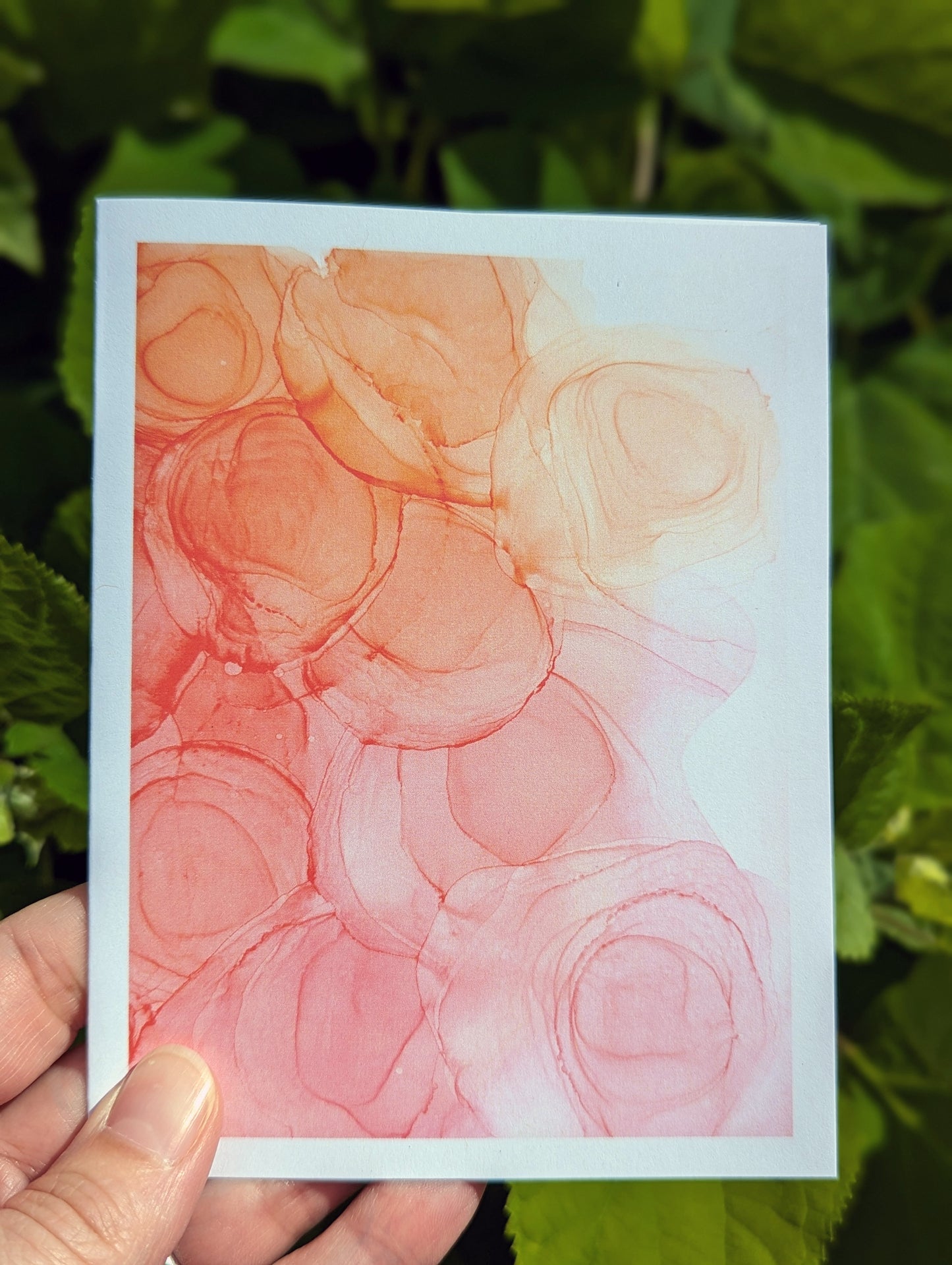 Hand holding a greeting card with green leaves in the background.