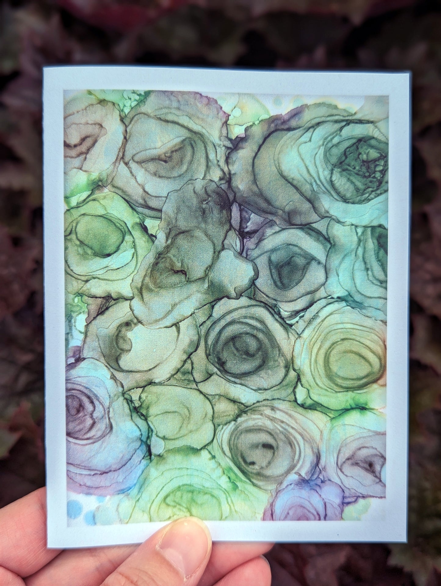 Hand holding a greeting card with greenery in the background.