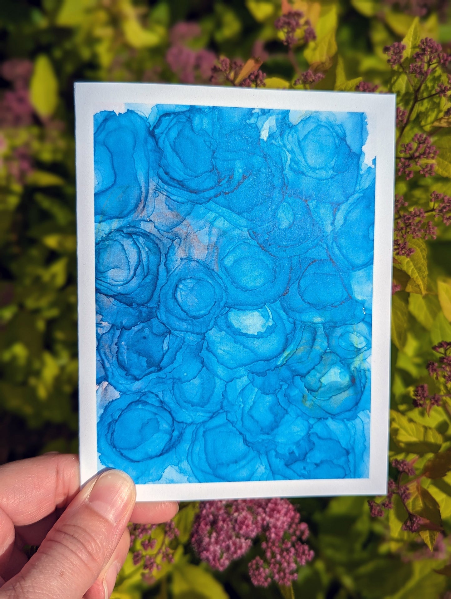 Hand holding a greeting card with green leaves in the background.