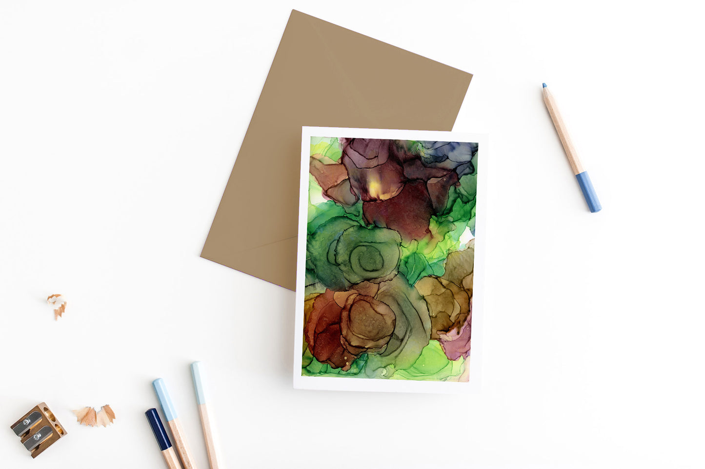 Greeting card, seen from above, with a colored, square flap envelope, pencils, pencil sharpener and shavings on a white background.