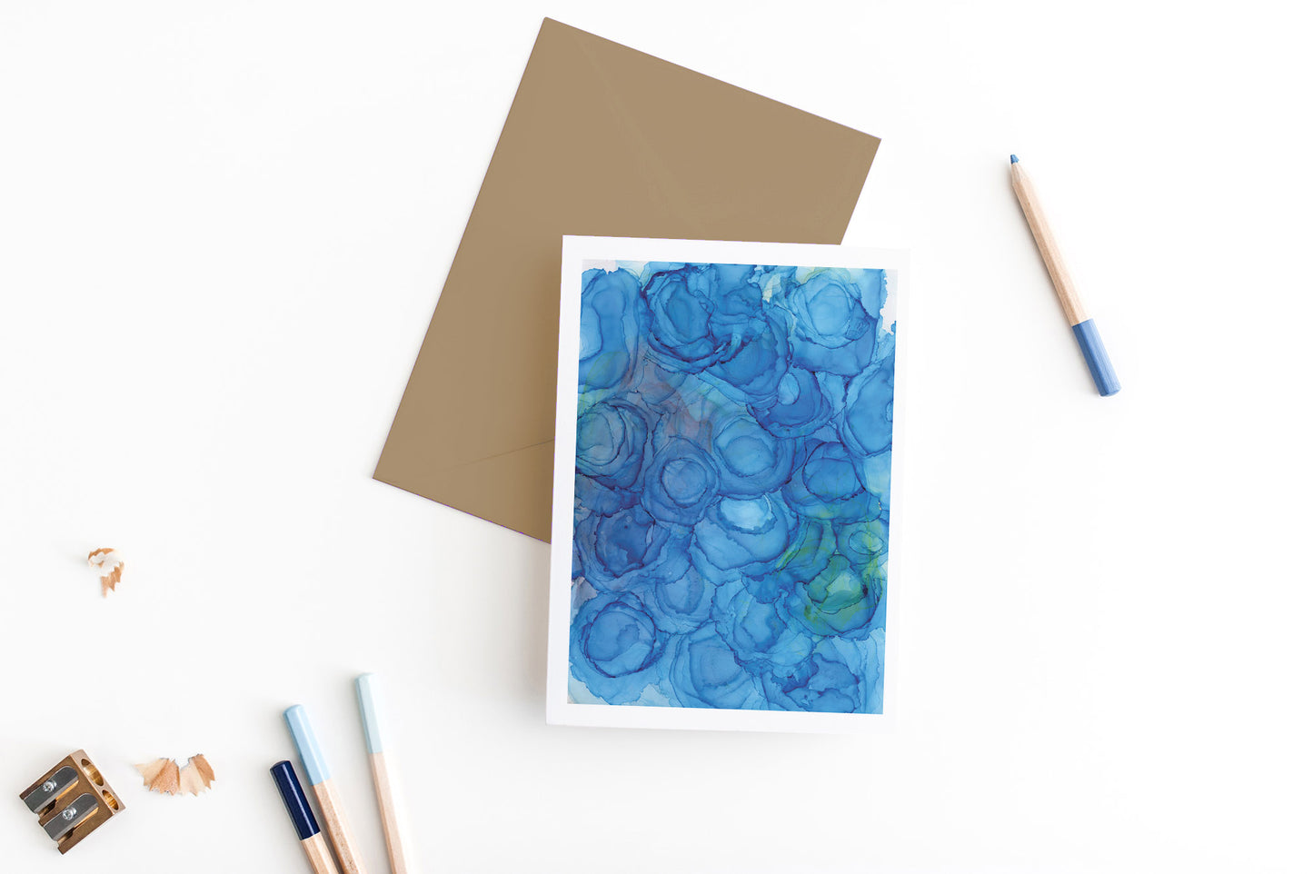 Greeting card, seen from above, with a colored, square flap envelope, pencils, pencil sharpener and shavings on a white background.