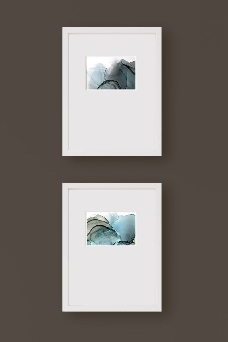 Zoomed in detail of two paintings framed in white against a brown wall.