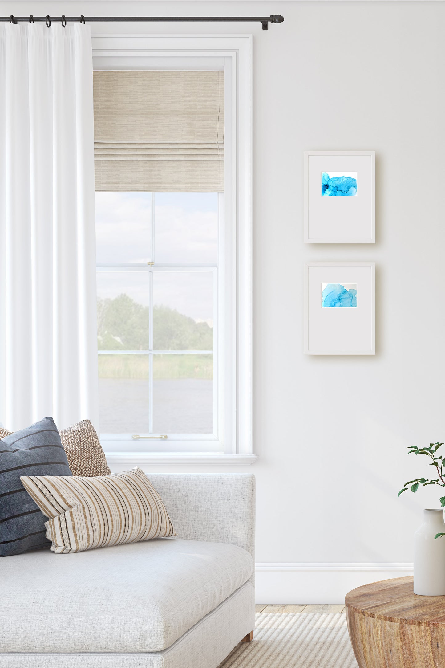 Digital mockup of two paintings hung on a light grey living room wall next to a window. A sofa and coffee table are in the foreground.