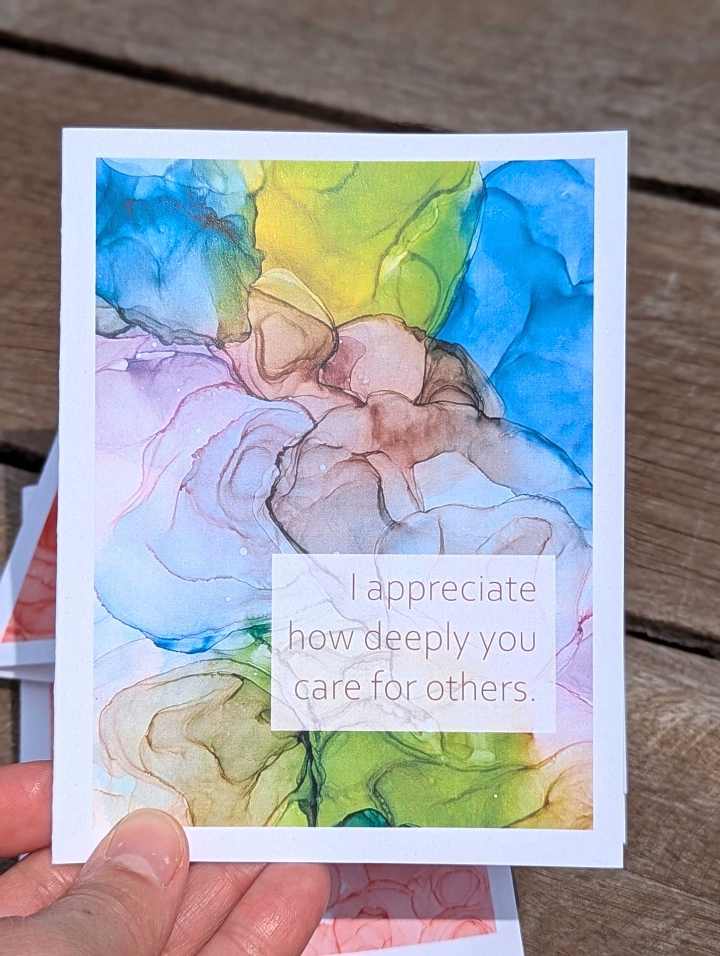 Colorful flowy ink art card with a message held above a wooden surface.