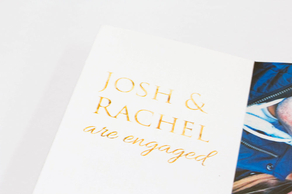 Centerpiece laying flat on a white background showing the couple's names and the words are engaged as well as a portion of a picture of the couple.