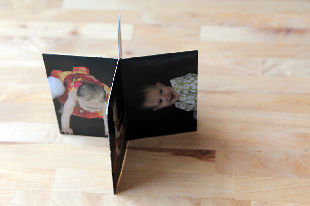 Overhead view of a centerpiece standing on a wooden table top. The photos show a toddler sitting smiling at the camera and pushing up to a stand.