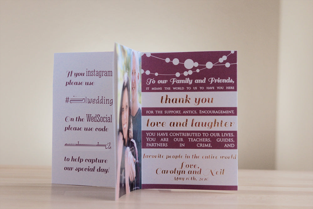 Centerpiece standing on a wooden table with a white wall in the background. The panels show social media hashtag instructions, an engagement photo, and a thank you note to attendees from the couple.