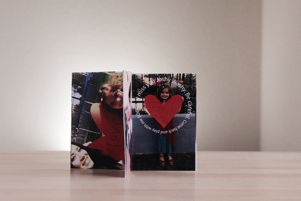 Centerpiece standing on a wooden table top with panels showing a child holding a large paper heart and a personal message to the soldier who will have this folded keepsake when they are away from home.