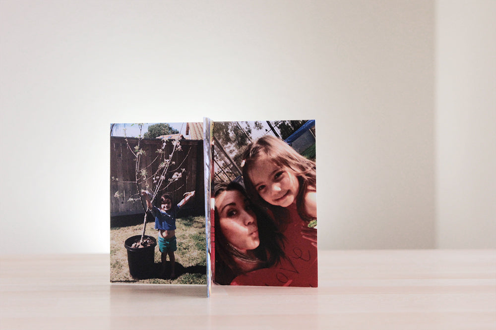Centerpiece standing on a wooden table top showing photos of a child holding onto a young potted tree waiting to be planted and a young adult and child with a paper heart blowing kisses to the camera.