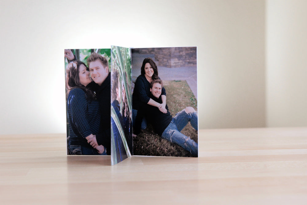 Centerpiece standing on a wooden table. The panels show engagement photos of a couple dressed in navy and jeans smiling into the camera.