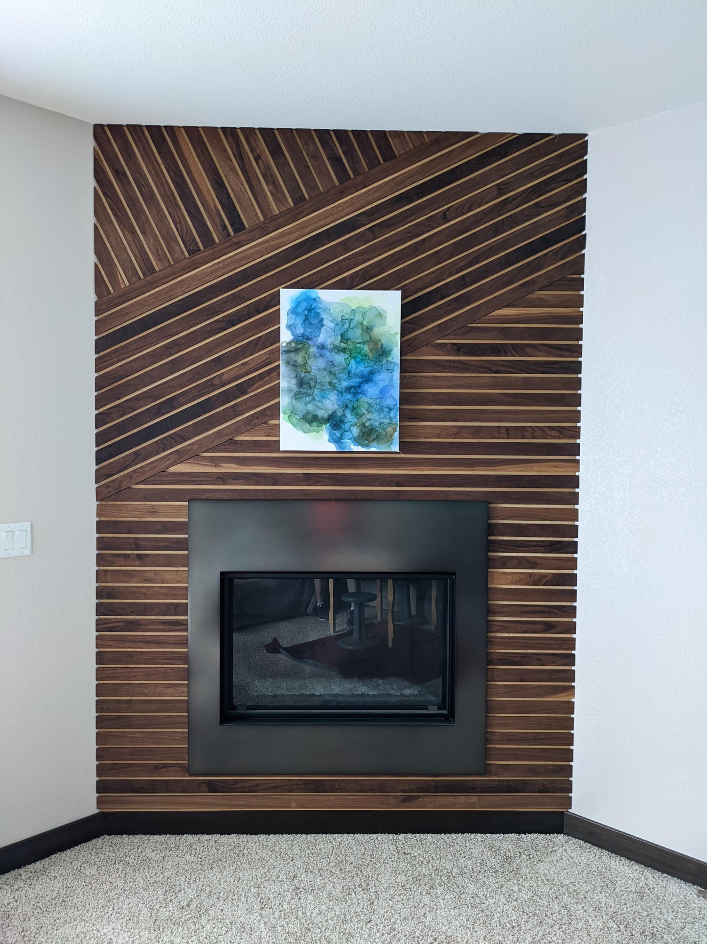 One canvas shown above a fireplace against a wood slat wall.