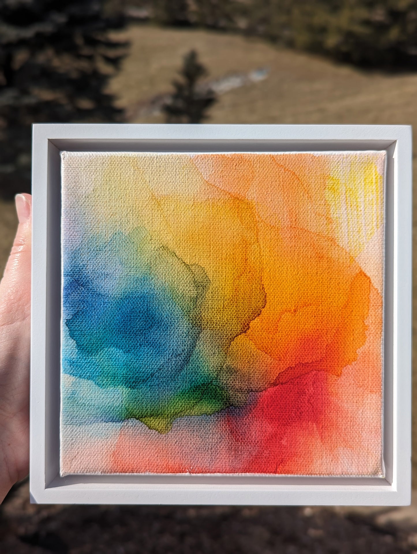 Hand holding the white float framed And the Promise of Sunshine outdoors.