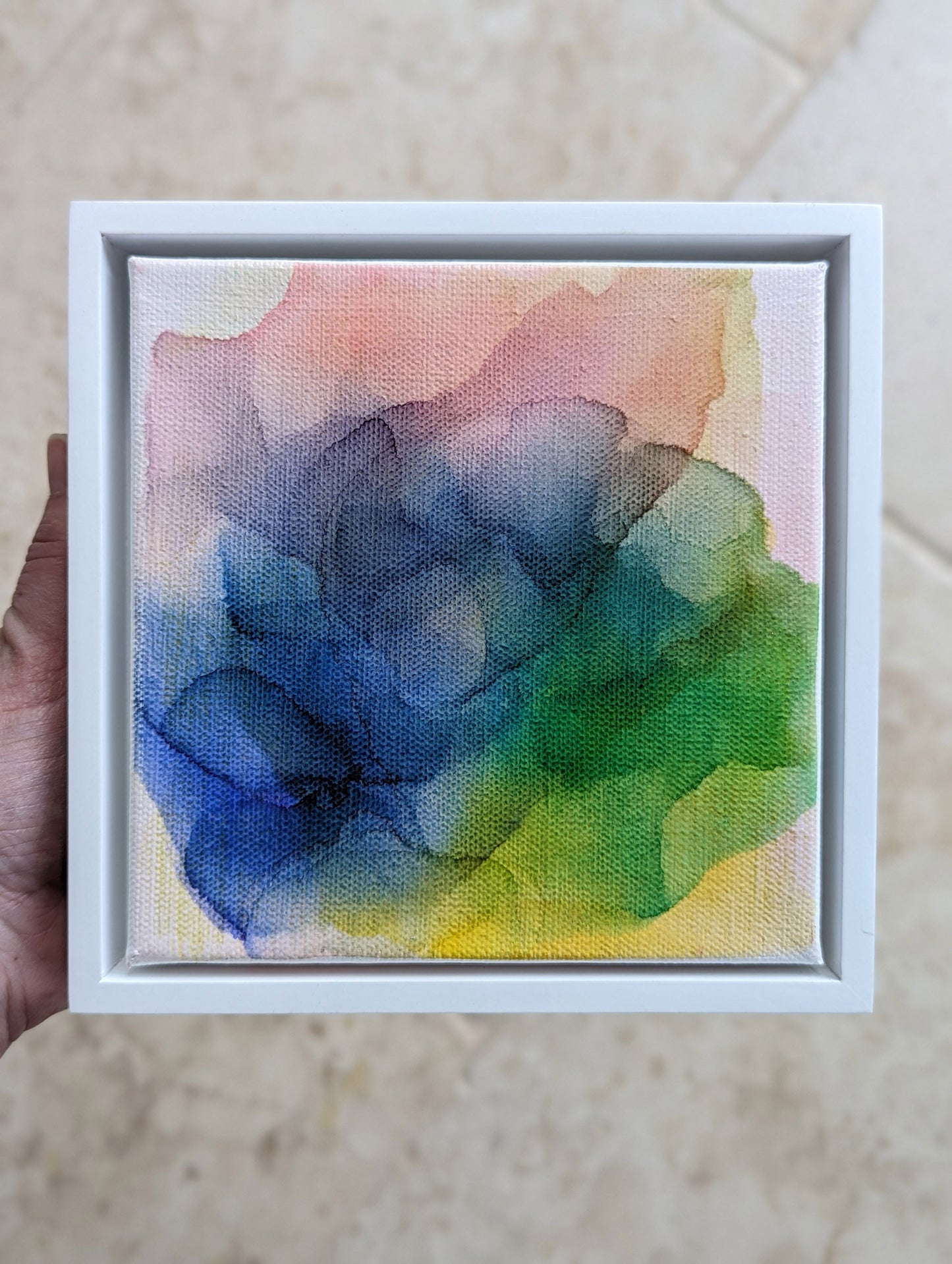Hand holding the white float framed Enduring Joys indoors.