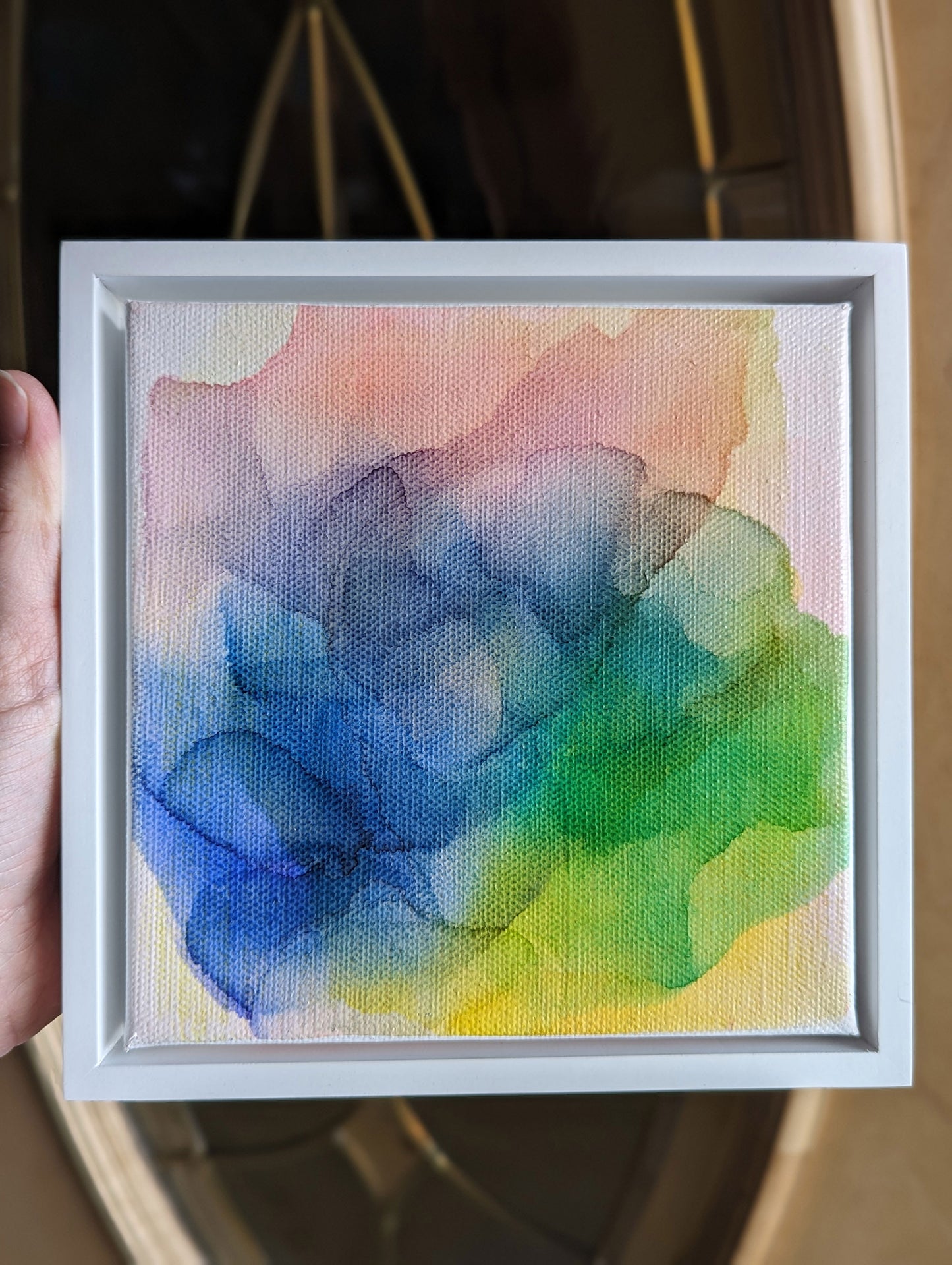 Hand holding the white float framed Enduring Joys with light coming in from a doorway.