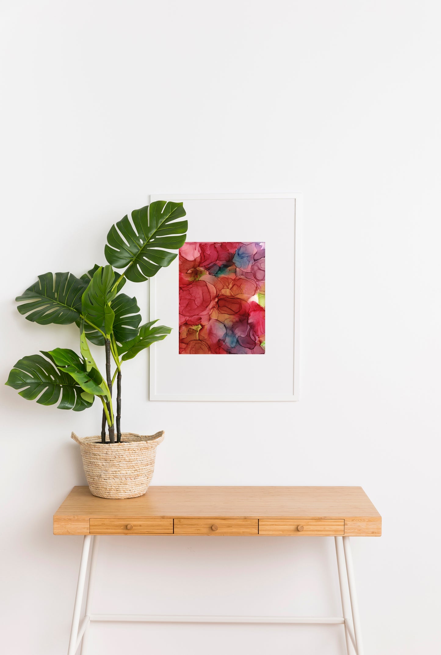 Zoomed out digital mockup of A Day of Happiness framed in white hanging on a white wall. A tropical plant potted in a woven basket sits on a wooden console table in the foreground.