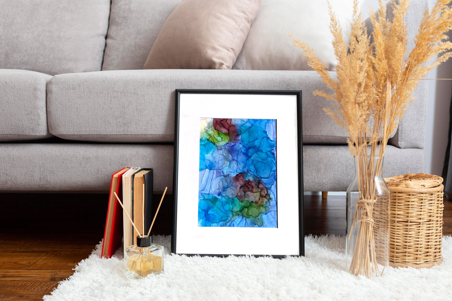 Digital mockup of Balancing Ease and Effort framed in black leaning on a white rug against the base of a light grey sofa. Books, incense sticks, a woven basket, and dried plants in a clear vase accessorize the space.