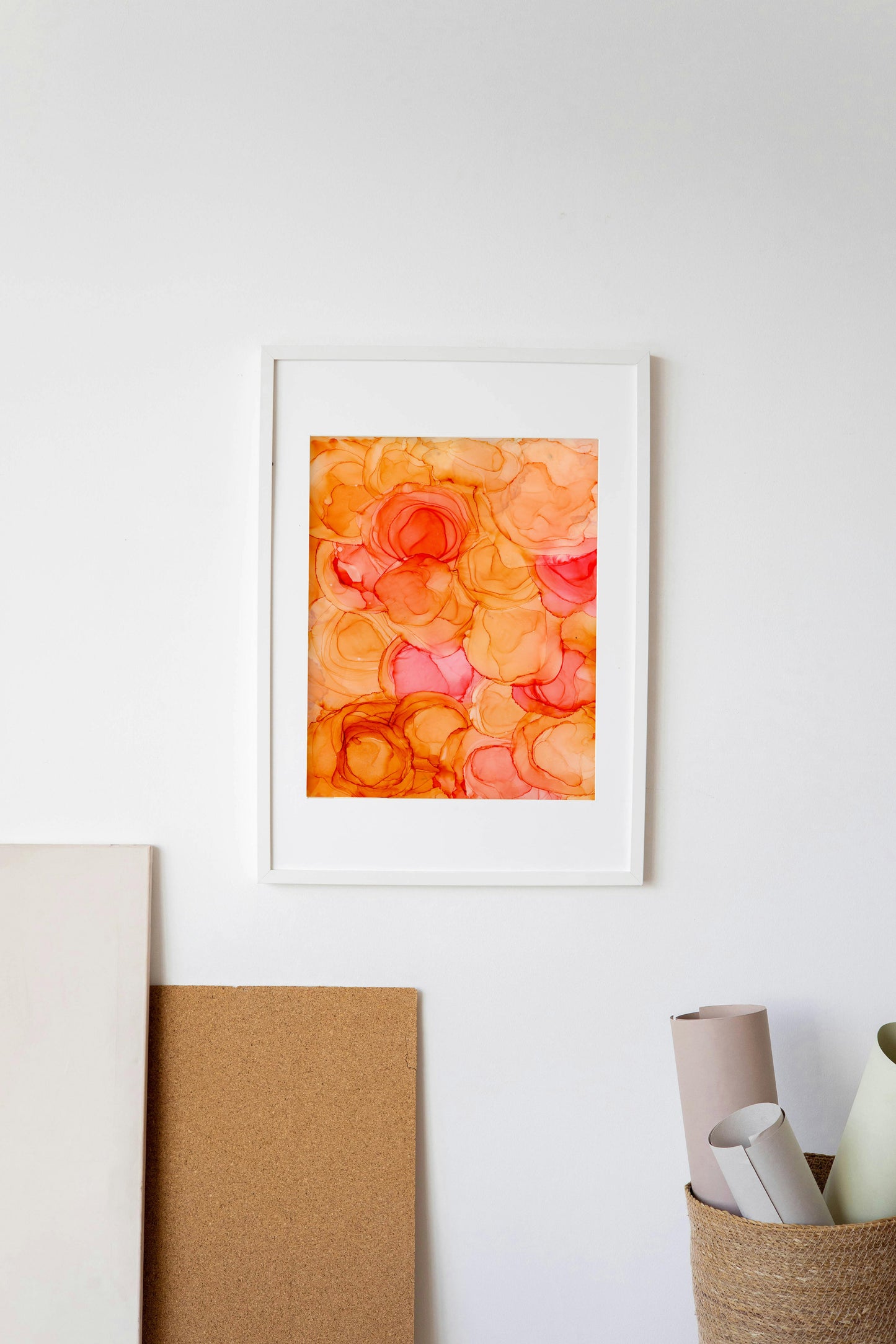 Digital mockup of Blooming + Growing framed in white hung on a white wall with a basket of rolled paper and a sheet of cork below.