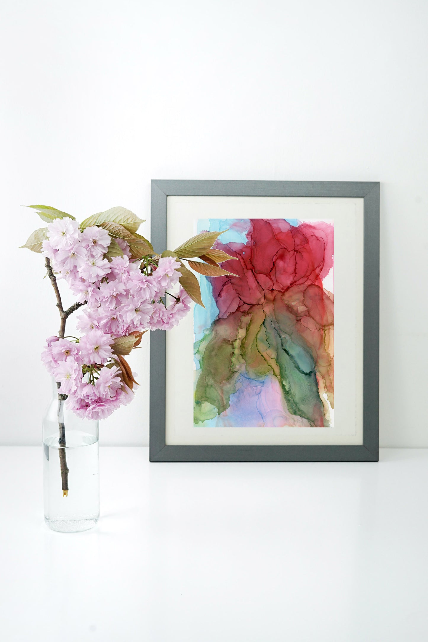 Digital mockup of Capable of Amazing Things framed in silver with a white background. A clear vase with a flowering branch sits to the side.
