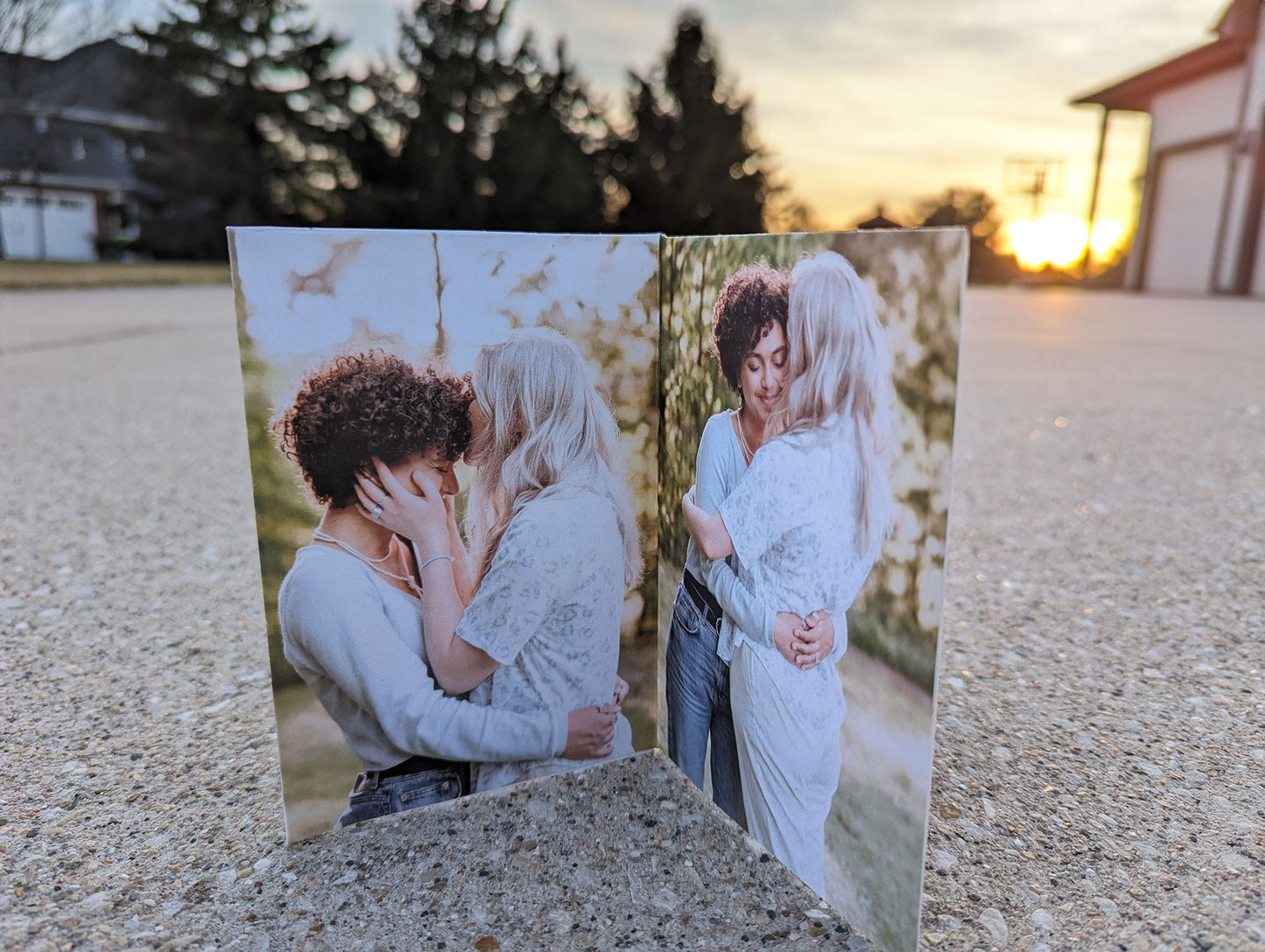 Centerpiece sitting on concrete with a sunset in the background showing photos of an LGBTQ+ couple hugging and one kissing the other on their forehead with hands along their face.