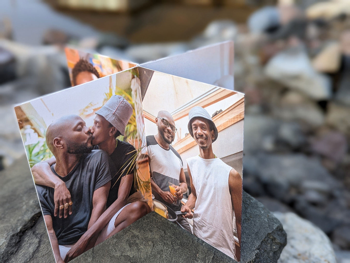 Cenerpiece sitting on rocks showing photos of an LGBTQ+ couple kissing and another where they are making breakfast in their kitchen and smiling at the camera.
