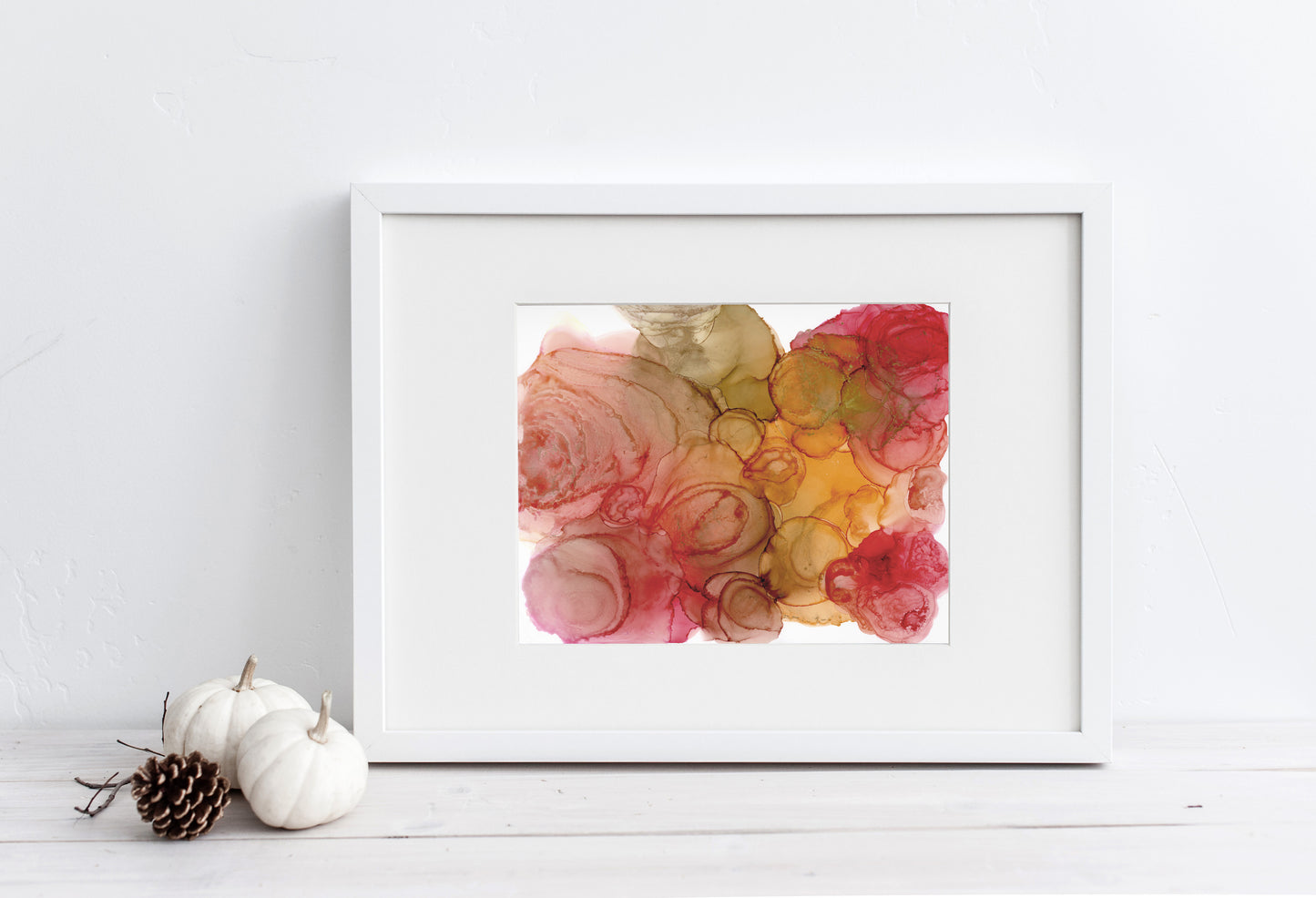 Digital mockup of Cycle of the Season framed in white sitting horizontally on white boards leaning against a white wall. Small white pumpkins and pinecone sit off to the side.