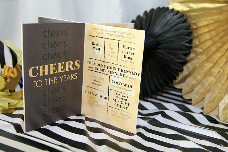 Closeup of a black and gold table centerpiece on a black and white striped tablecloth with black and gold paper medallions off to the side.