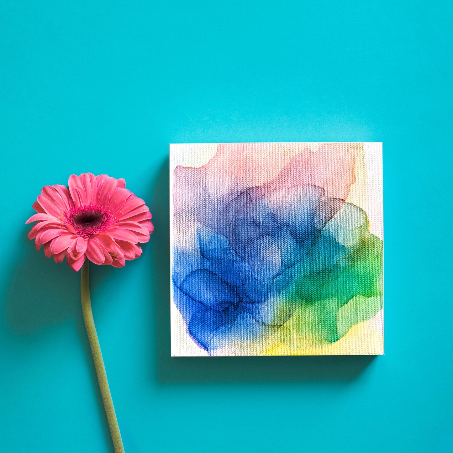 Digital mockup of the canvas laying on a teal backgorund next to a single pink flower.