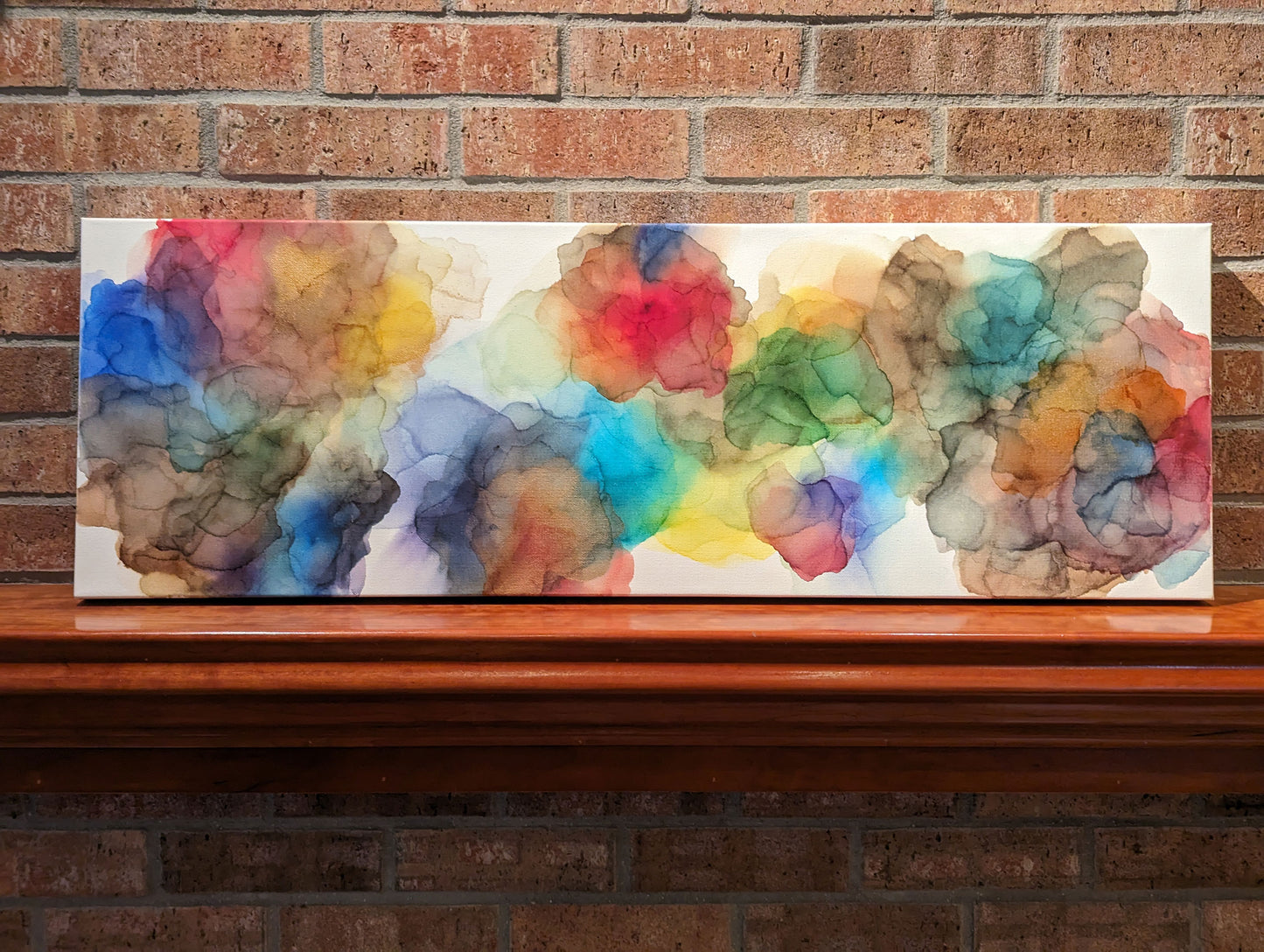 Horizontal orientation of Expanding Boundaries shown leaning on a wooden mantel against a brick fireplace.