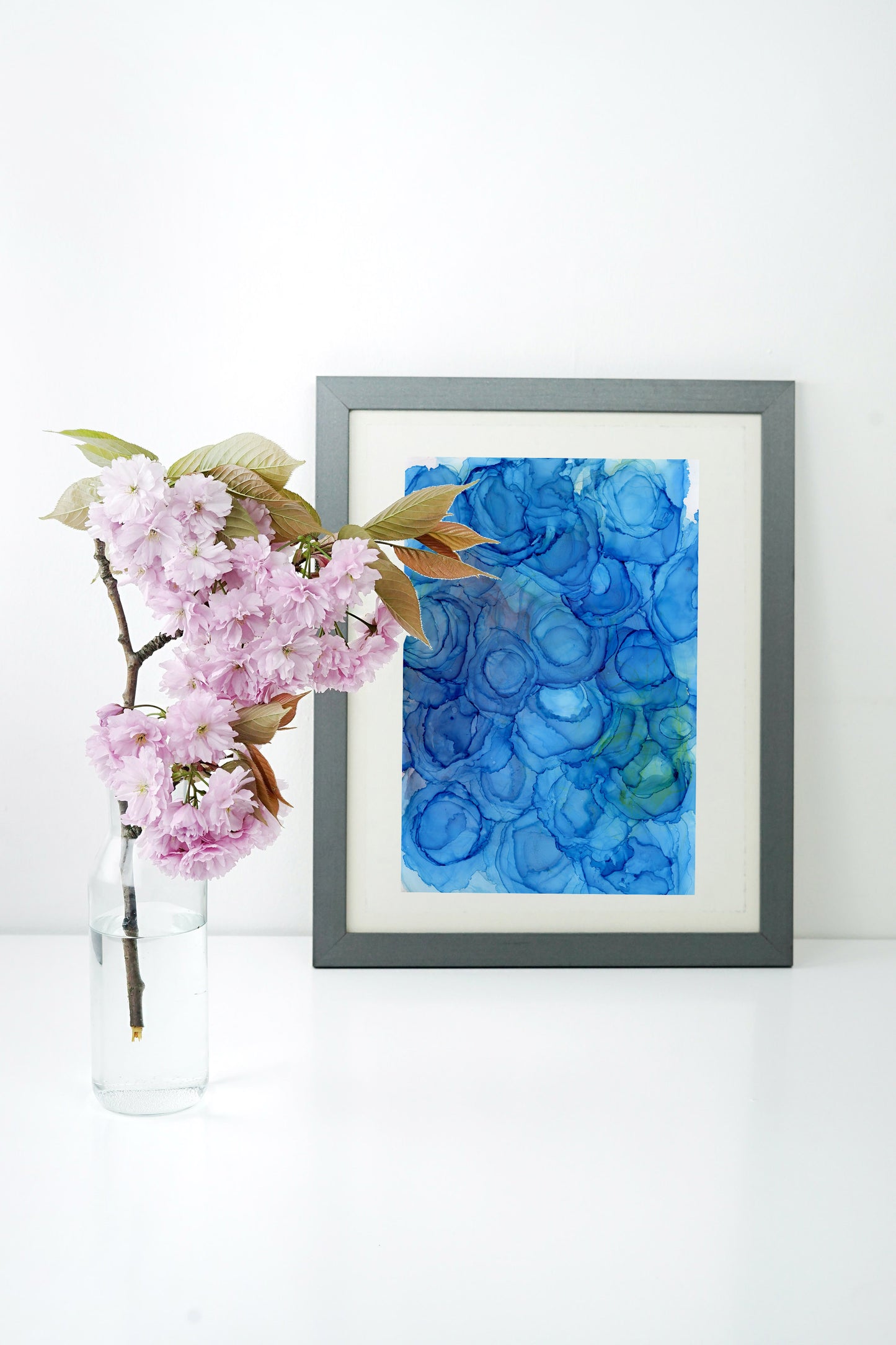 Digital mockup of Healing Energy framed in silver with a white background. A clear vase with a flowering branch sits to the side.