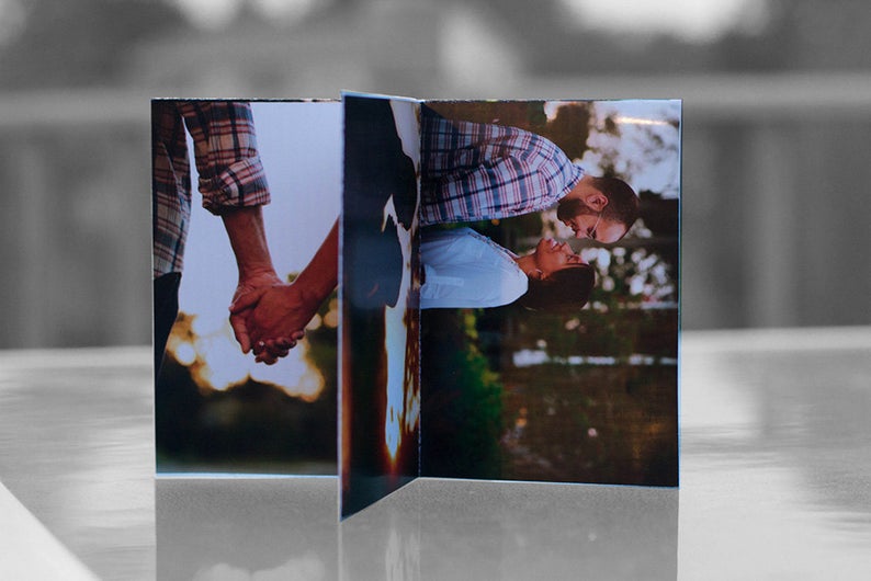 Centerpiece sitting on a glass table outdoors. The panels show engagement photos of a couple standing close to each other looking into each other's eyes and another of them holding hands.