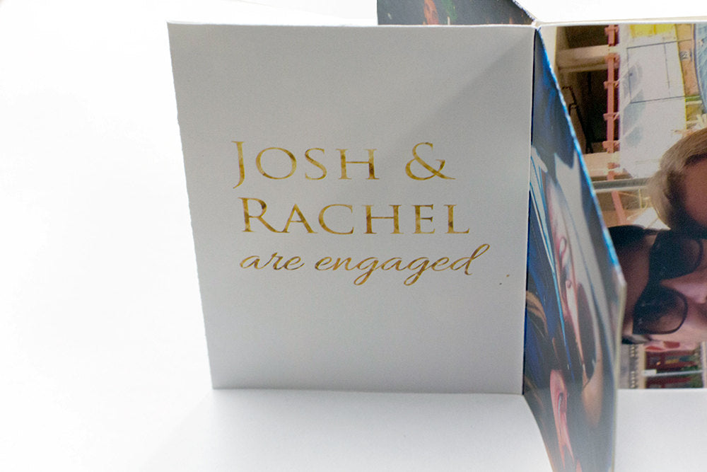 Centerpiece laying flat on a white background showing the couple's names and the words are engaged as well as a portion of a picture of the couple.