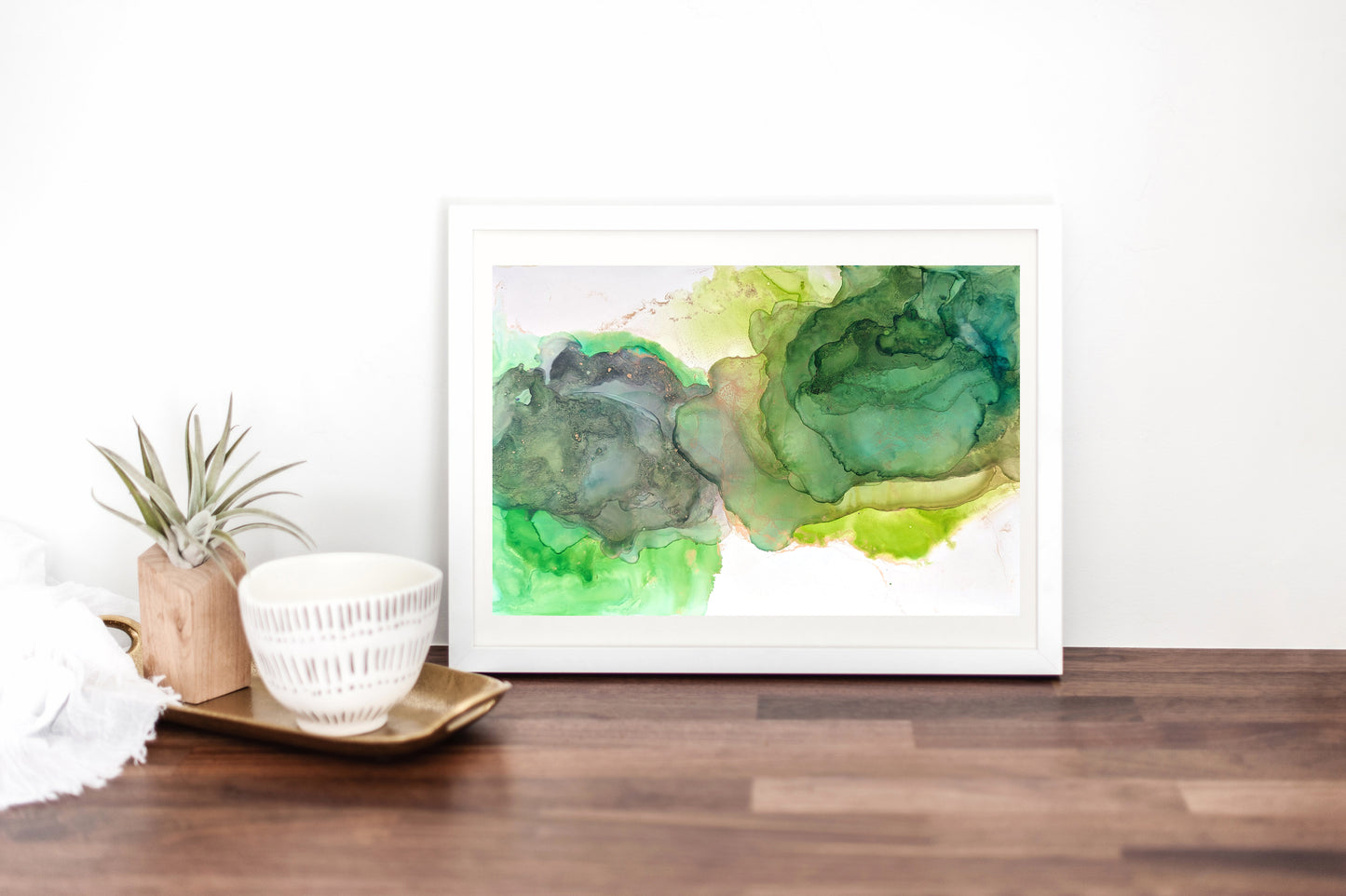 Digital mockup with Light Shines From Within framed in white on a wood table, leaned against a white wall. Some vessels and an airplant sit on a tray off to the side.